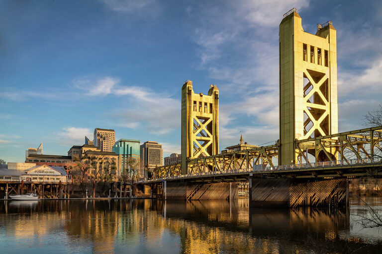 A yellow vertical lift bridge spans a river with a city skyline in the background under a partly cloudy sky—a scenic spot any pet lover or mobile pet grooming enthusiast would enjoy while out with their furry friend.