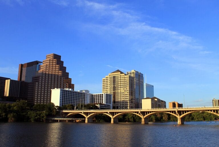 City skyline with modern buildings and a bridge over a river under a clear blue sky.